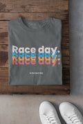 Gray t-shirt with 'Race day. Race day. Race day.' text in colorful letters on a wooden surface.