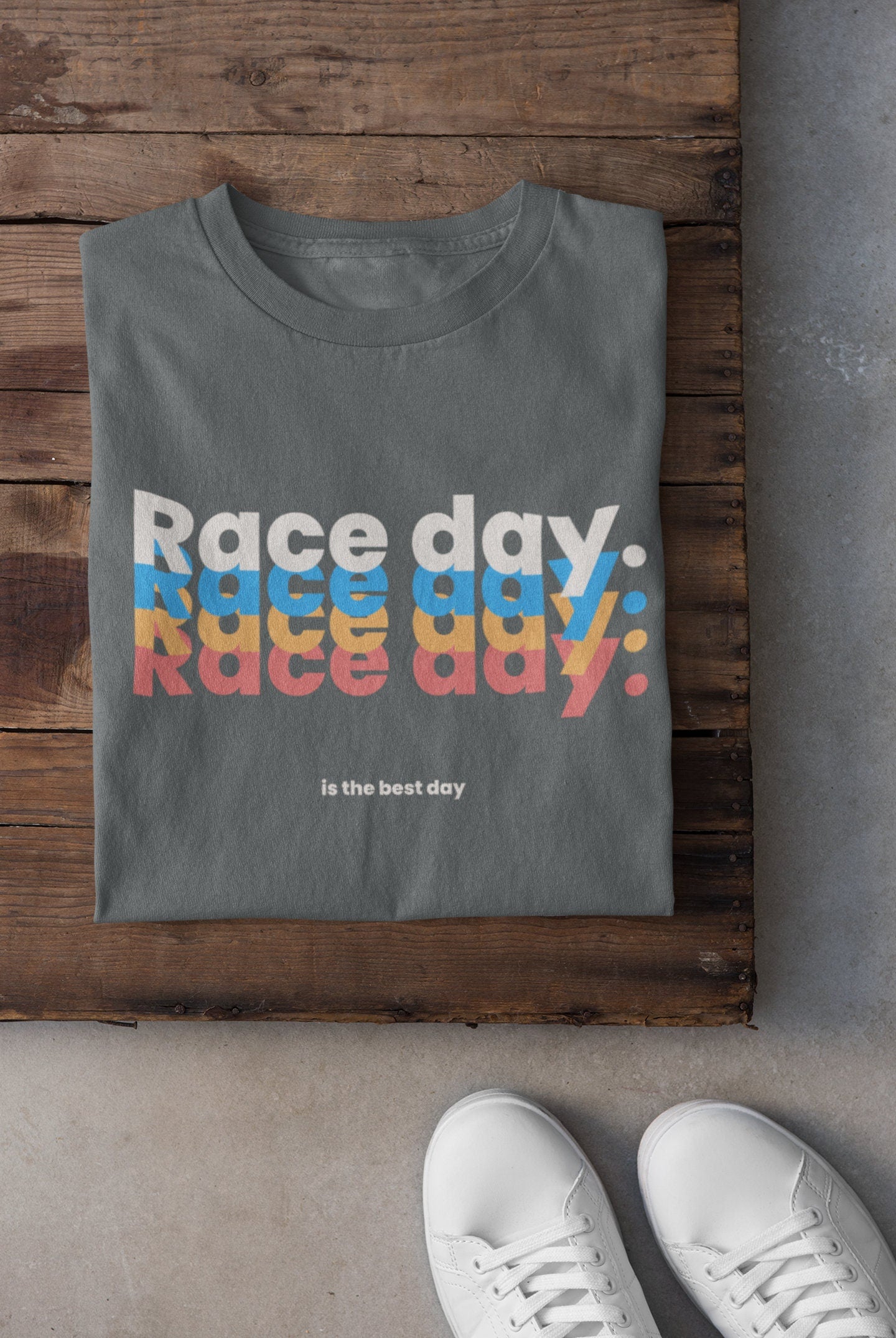 Gray t-shirt with 'Race day. Race day. Race day.' text in colorful letters on a wooden surface.