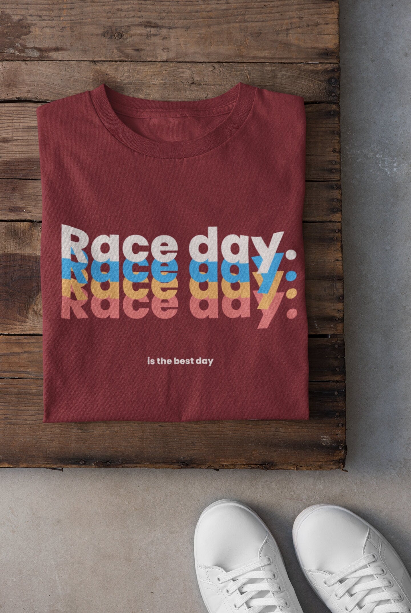 Maroon t-shirt with 'Race day, race day, race day' text on a wooden surface with white sneakers.