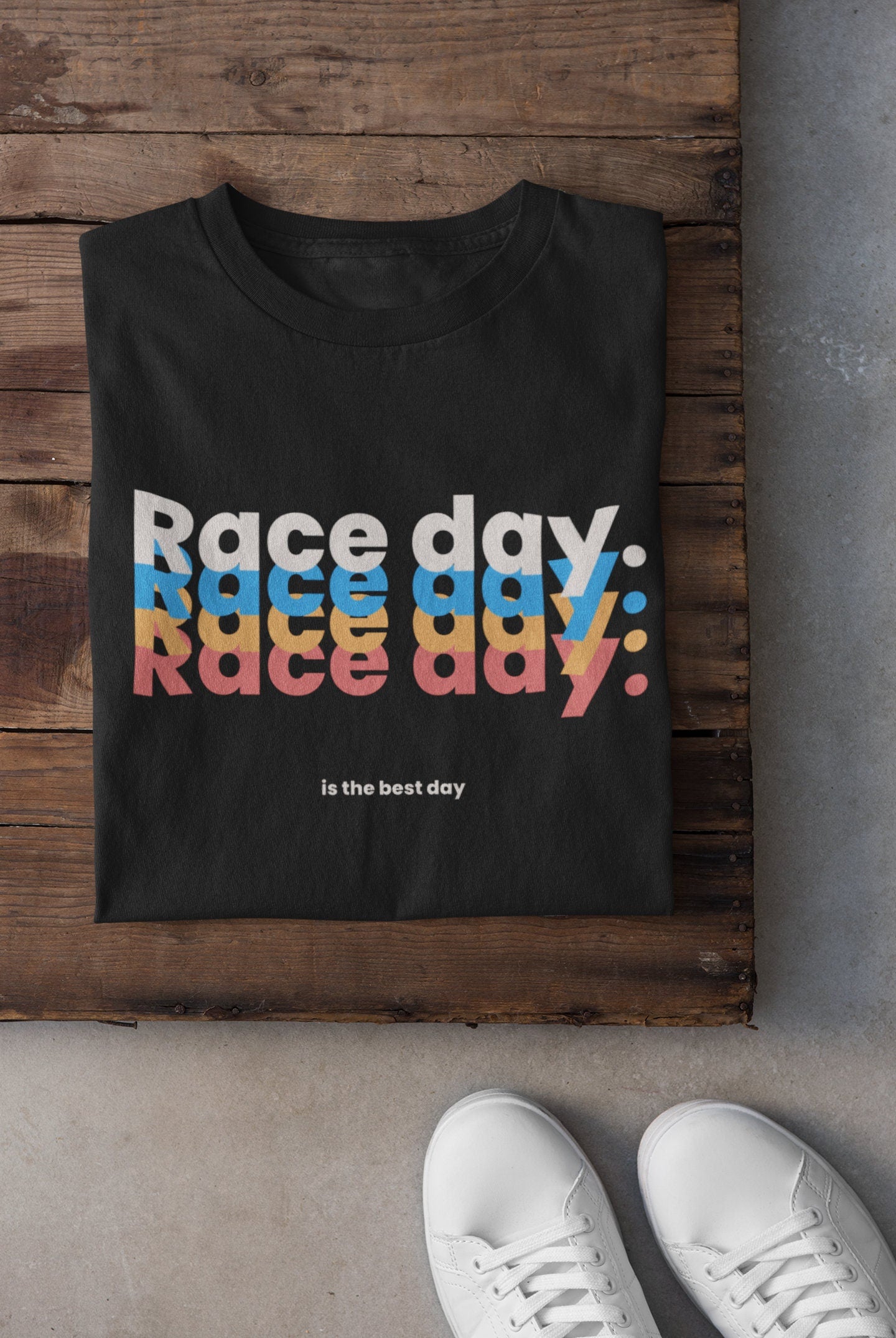 Black t-shirt with 'Race day, race day, race day' text in colorful letters on a wooden surface.