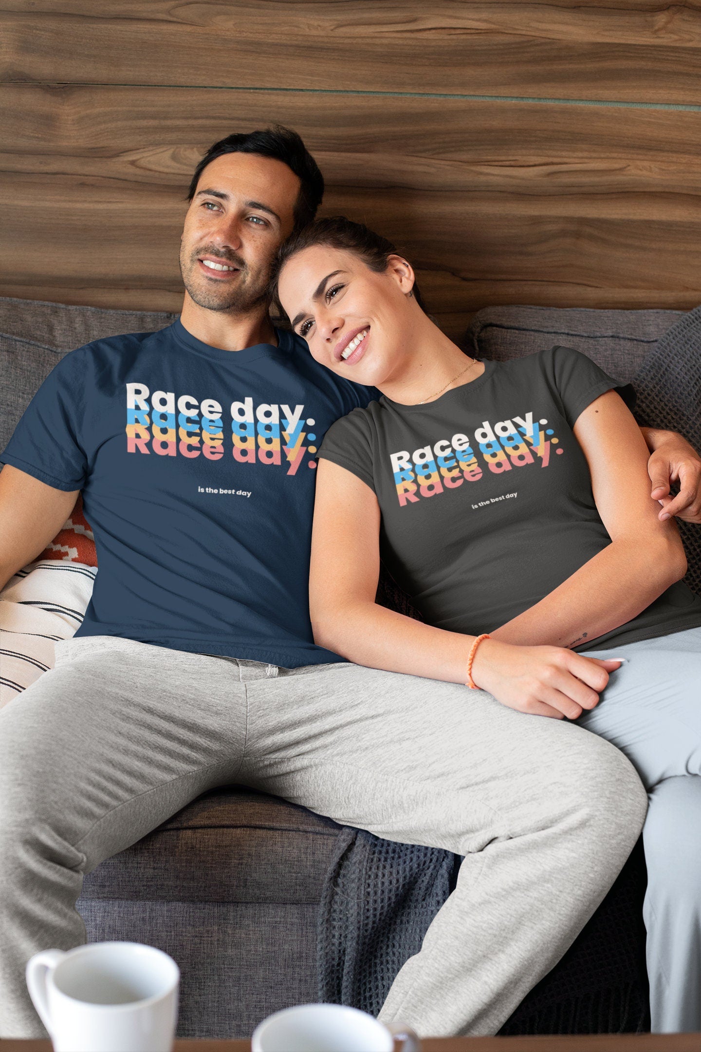Man and woman sitting on a couch wearing 'Race day' t-shirts with colorful text.