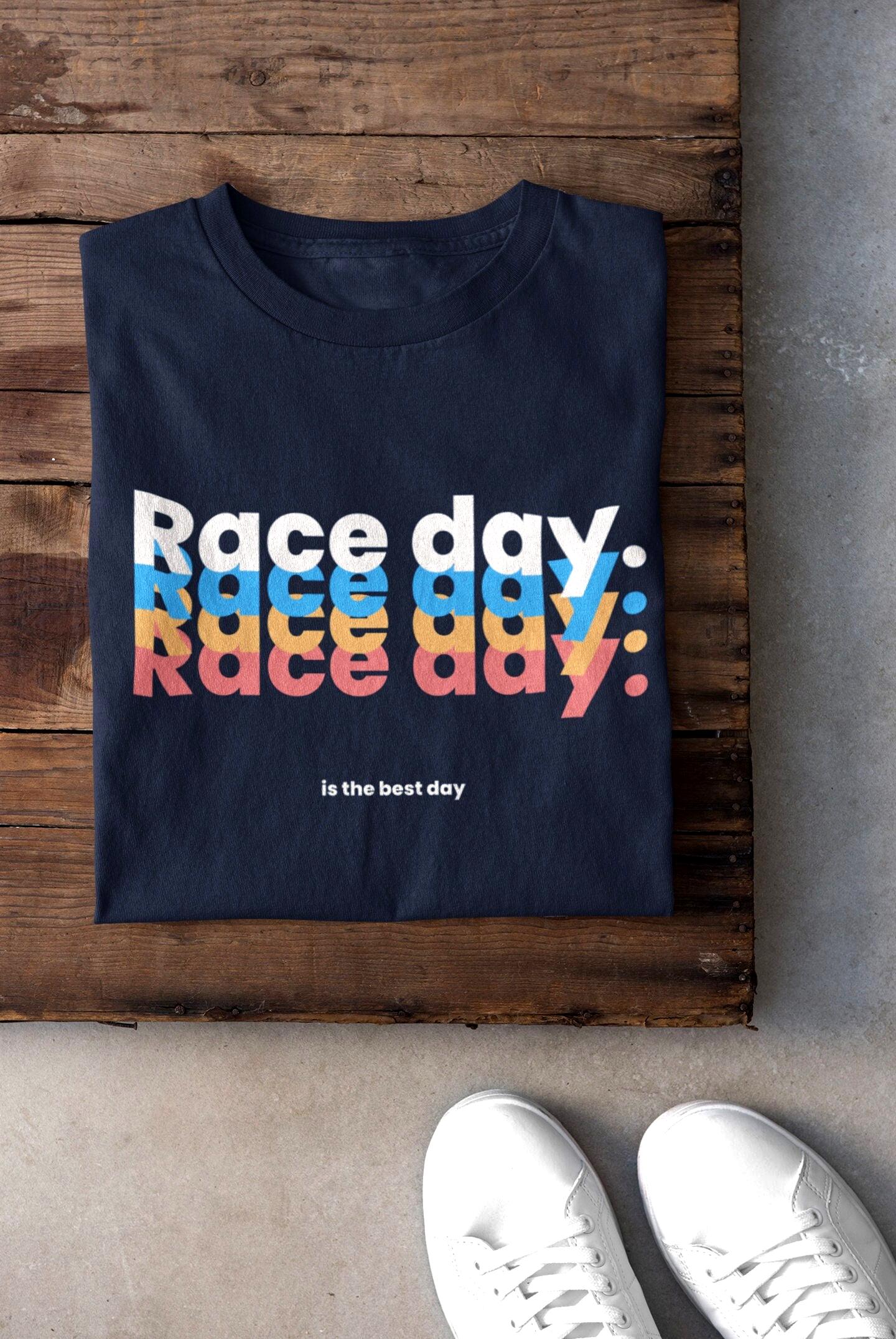 Navy blue t-shirt with 'Race day. Race day. Race day.' text in multicolor on a wooden surface.
