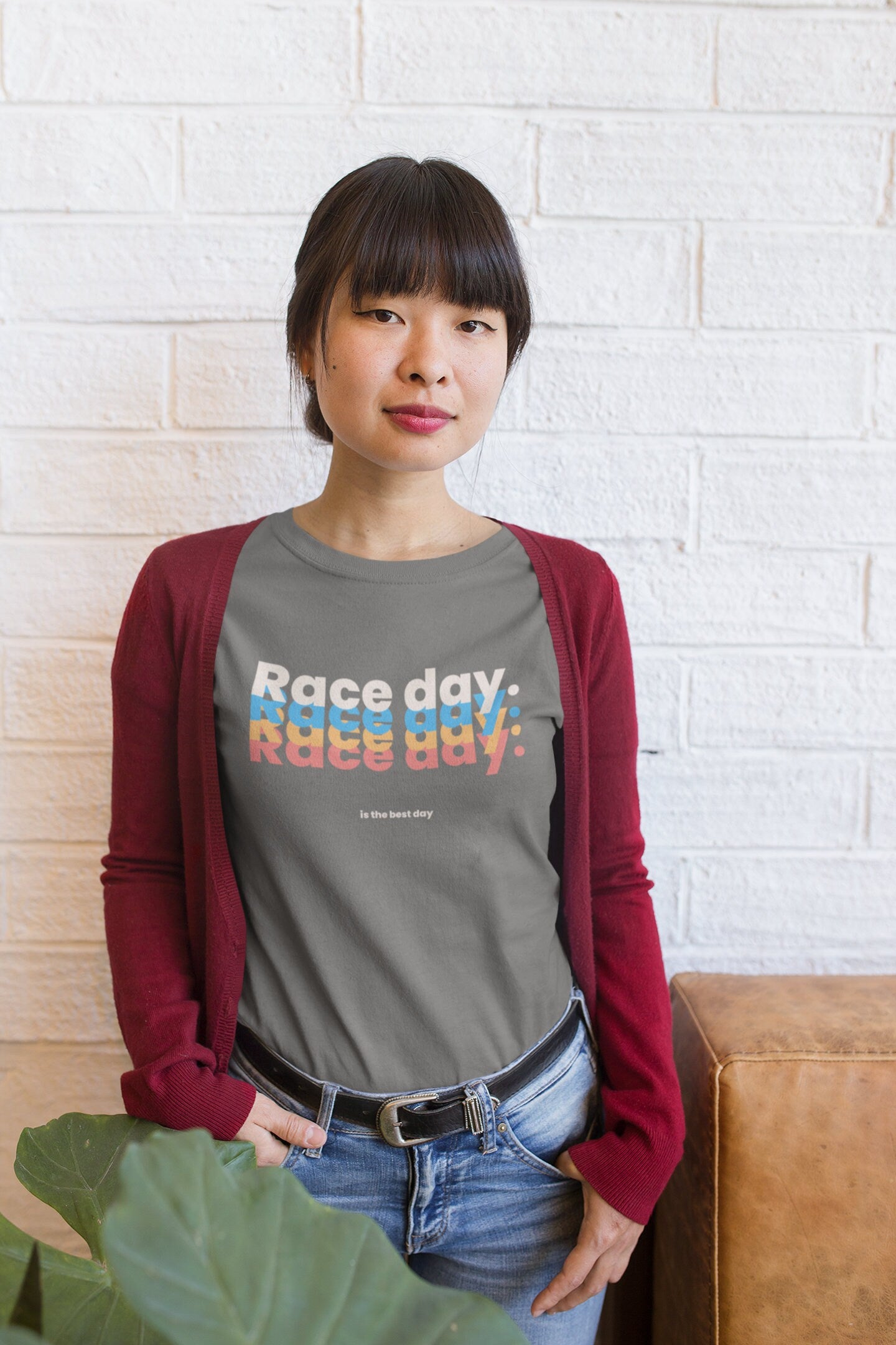 Person wearing a gray t-shirt with 'Race day, race day' text in front of a white brick wall.