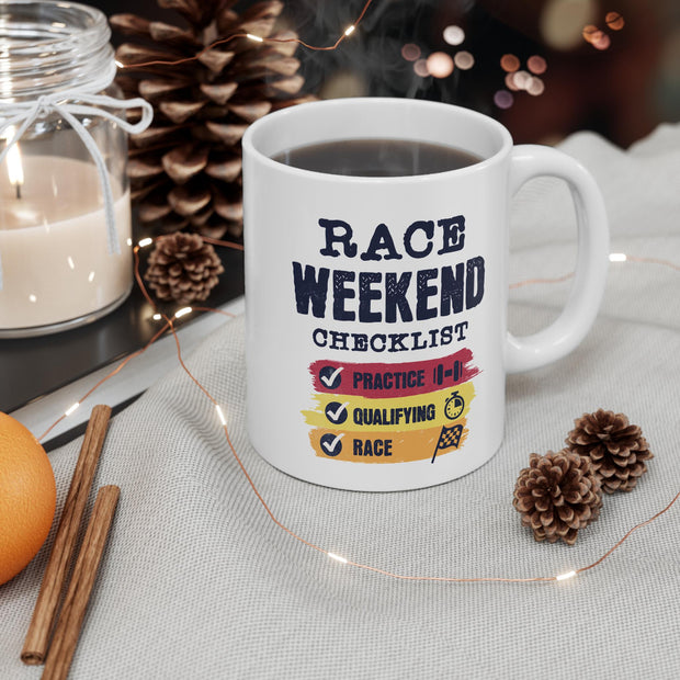 A white coffee mug with a black and red design that says 'Race Weekend Checklist' with checkmarks next to the words 'Practice', 'Qualifying', and 'Race'. The mug is sitting on a white and gray textured surface.
