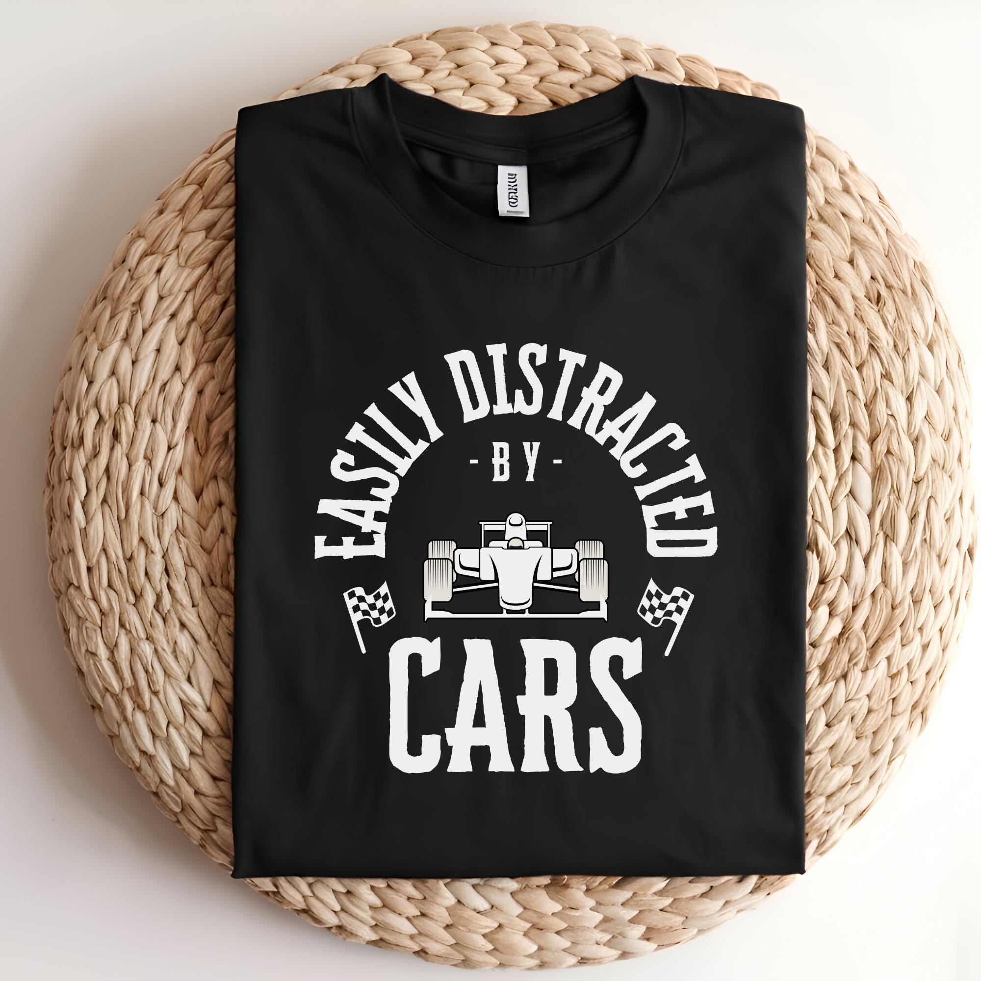 A black t-shirt with white text that reads 'Easily Distracted - By - Cars'. A white silhouette of a race car is in the center of the text.