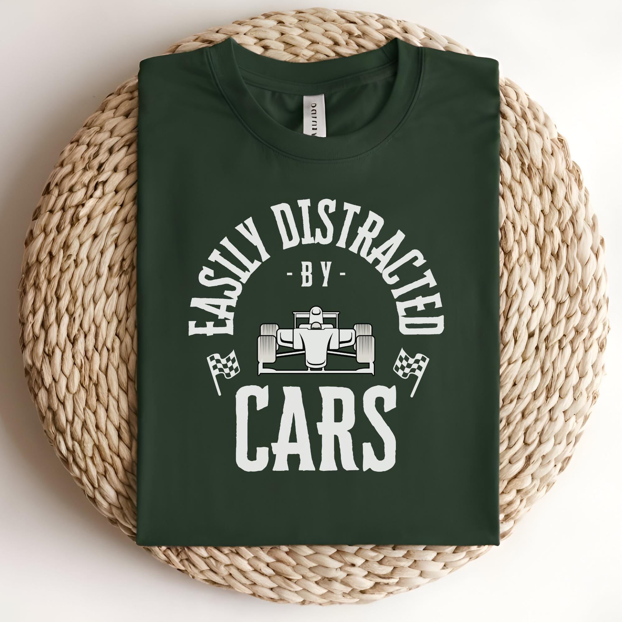 A green t-shirt with white text that reads 'Easily Distracted By Cars' with a white race car graphic in the center.