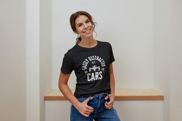 A young lady wearing  a black t-shirt with white text that reads 'Easily Distracted by Cars' with a small image of a race car in the center of the text.
