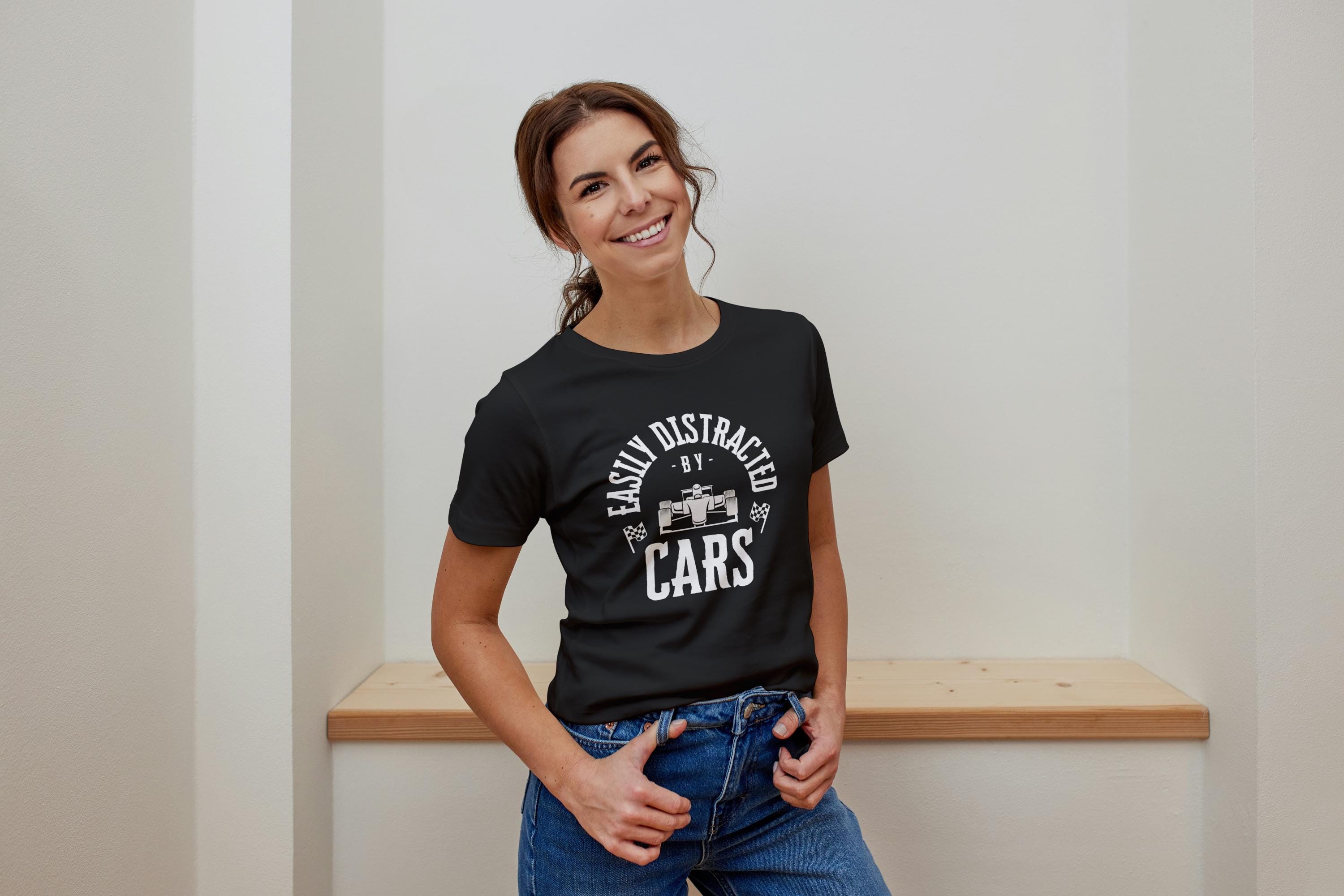A young lady wearing  a black t-shirt with white text that reads 'Easily Distracted by Cars' with a small image of a race car in the center of the text.