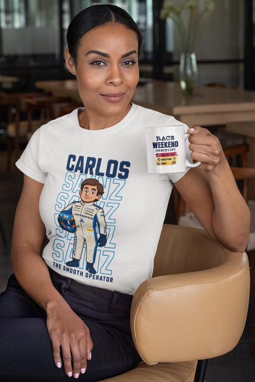 Woman wearing a white Carlos Sainz Smooth Operator cartoon T-shirt while holding a race weekend coffee mug, Formula 1 Williams fan merch.