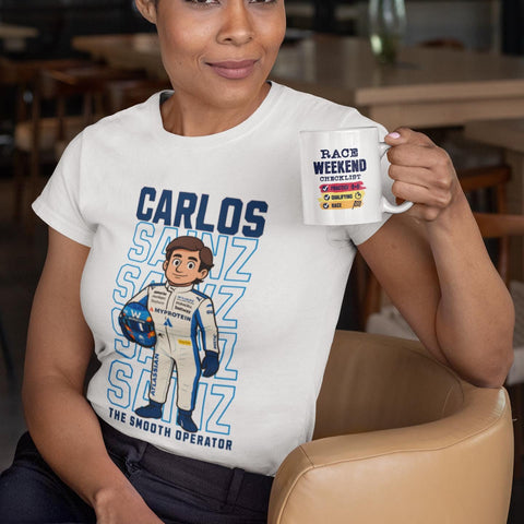 Woman wearing a white Carlos Sainz Smooth Operator cartoon T-shirt while holding a race weekend coffee mug, Formula 1 Williams fan merch.